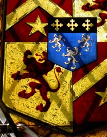 Heraldic stained glass in striking shades of red, blue and gold and incorporating lions rampant, chevrons, mullets and cross crosslets