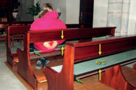 Congregation member warms her hands on a transparent glass heating panel between the pew's back-rail and seat