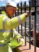 A man in a hard hat and high vis jacket painting railings in situ
