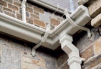 Cast iron gutters and square-section downpipes supported off slender strap brackets and with off-white paint finish