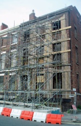 Three storey brick facade supported by scaffolding and timber boards fixed to wall face