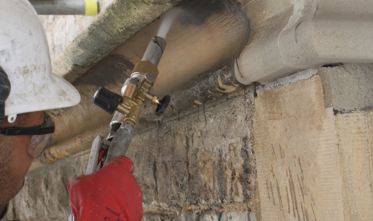 An operative in hard hat and safety glasses operates a swirling vortex abrasive system