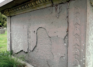 The stone surface of a chest tomb's side panel separates from the substrate in a thin fragile layer