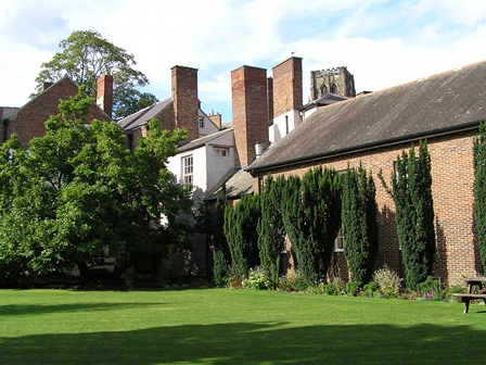 Lawn, flower borders and evergreen trees with red-brick and white rendered buildings in background