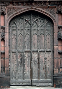 Timber double door with detailed gothic decoration and decayed weatherboard at base