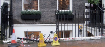 Damaged railings with one buckled and broken section lying on the plinth surrounded by traffic cones