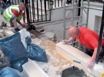 Workmen position a new section of stone plinth using a string line