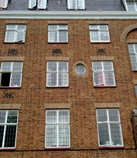 Brick facade with rectangular four-light steel windows under flat arches; single oval window also shown