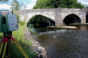 Survey equipment set up at historic stone road bridge