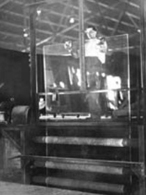 b/w photo showing sheet glass passing through rollers in the Fourcault Process