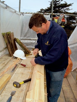 A joiner at a makeshift work-bench on a shrouded scaffolding platform