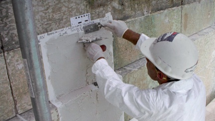 A conservator in protective clothing applies a cleaning poultice to a trial area