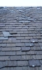 Slate roof with missing and slipped slates and some slates held in place by metal clips