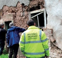 Experts inspect an area of clay wall fringed by the remains of the cement render, much of which has detached