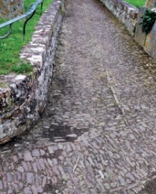 Cobbled path between low masonry walls with small sunken area darkened by damp