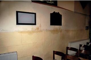 Irregular damp stains about four feet up an interior wall and following the horizontal line where cement render meets an earlier, lime-based plaster