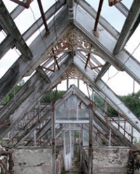 Decaying interior of derelict free-standing glasshouse with right-angle spandrel brackets at roof ridge