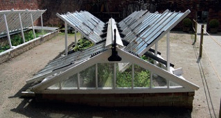 Triangular-section cold frame with hinged, glazed panels propped open (painted white)