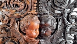Two carved putti heads surrounded by carved foliage: half of the panel has been cleaned and is a mellow light brown, the uncleaned half is close to ebony black