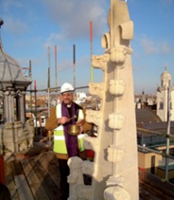 Rev’d Rob Gillian, wearing hard hat and high-visibility vest, blessing the new front finial