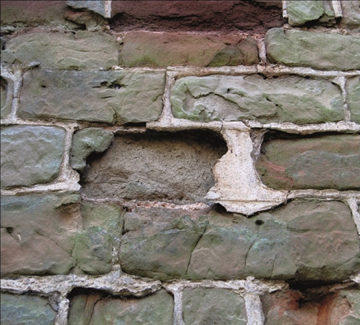 A wall with deteriorating stones and uneven mortar
