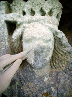 A conservator removes lichen from a stone sculpture