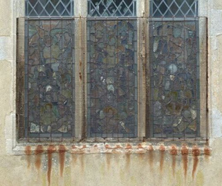 Stained glass window behind metal grille; rust streaks to stonework below