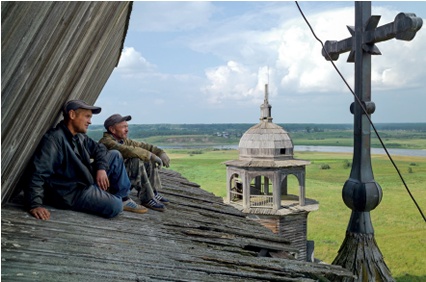 Two carpenters perch in the angle of a timber church roof, admiring the view