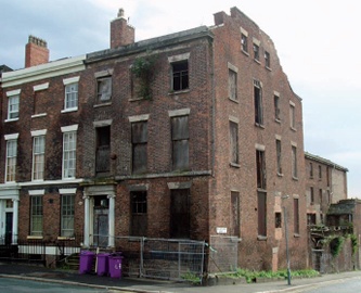 Regency end-of-terrace house in poor condition with missing or boarded up windows and plant growth at second floor level