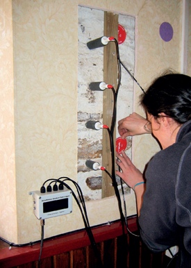 Monitoring equipment is attached to a section of the interior face of a wall from which the wallpaper and plaster has been removed to expose the stonework beneath