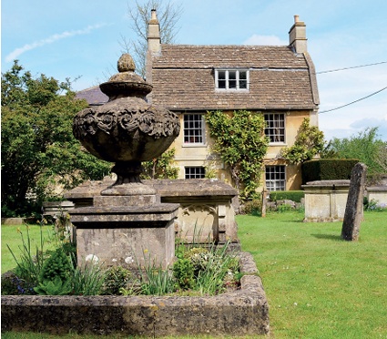 Churchyard monuments, chest tombs and gravestones with a historic gambrel-roofed house in the background