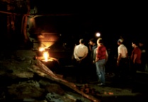 Men in shirtsleeves stand near glowing furnace