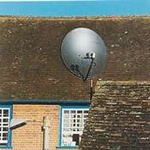 Unsympathetically installed black satellite dish on historic roof gable