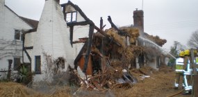 Firefighters direct a hose at the remains of a thatched roof